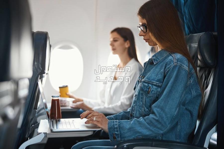 تذاكر الطيران بالاسعار الحقيقية كيف احصل عليها؟ سيدتان داخل طيارة واحداهما تستخدم اللابتوب الخاص بها