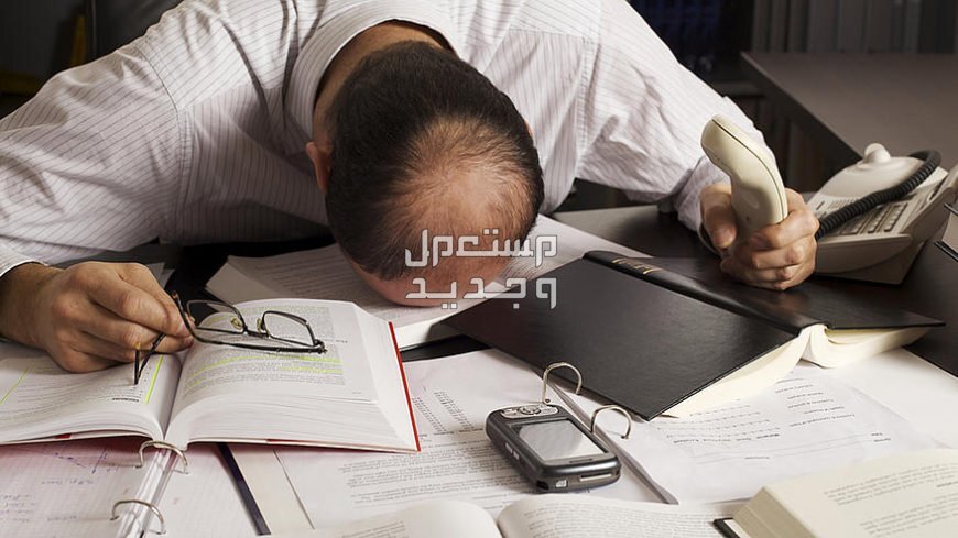 كيف تحمي نفسك من الاحتراق الوظيفي؟ رجل يشعر بالتعب ويضع راسه على المنضدة وسط الاوراق