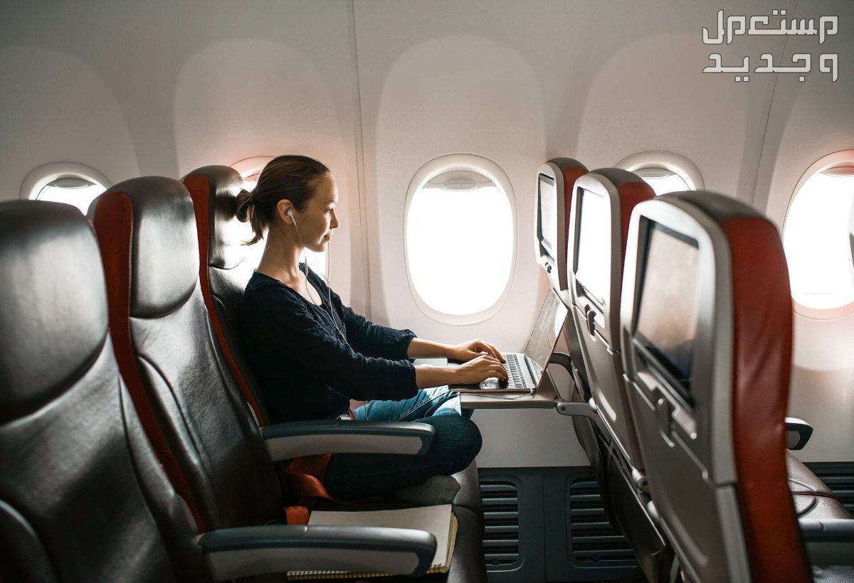 كيفية حجز تذكرة طيران في السعودية 1445 مسافرة تجلس بجانب النافذة وتستخدم اللاب توب الخاص بها