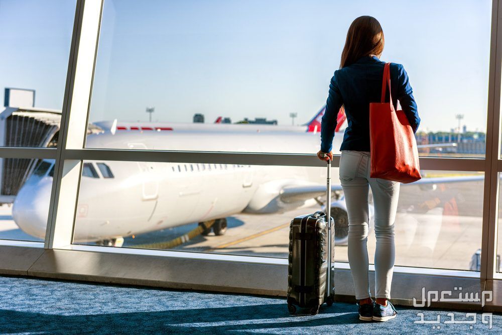 كيفية حجز تذكرة طيران في السعودية 1445 امراة تقف امام الطائرة ومعها حقائبها